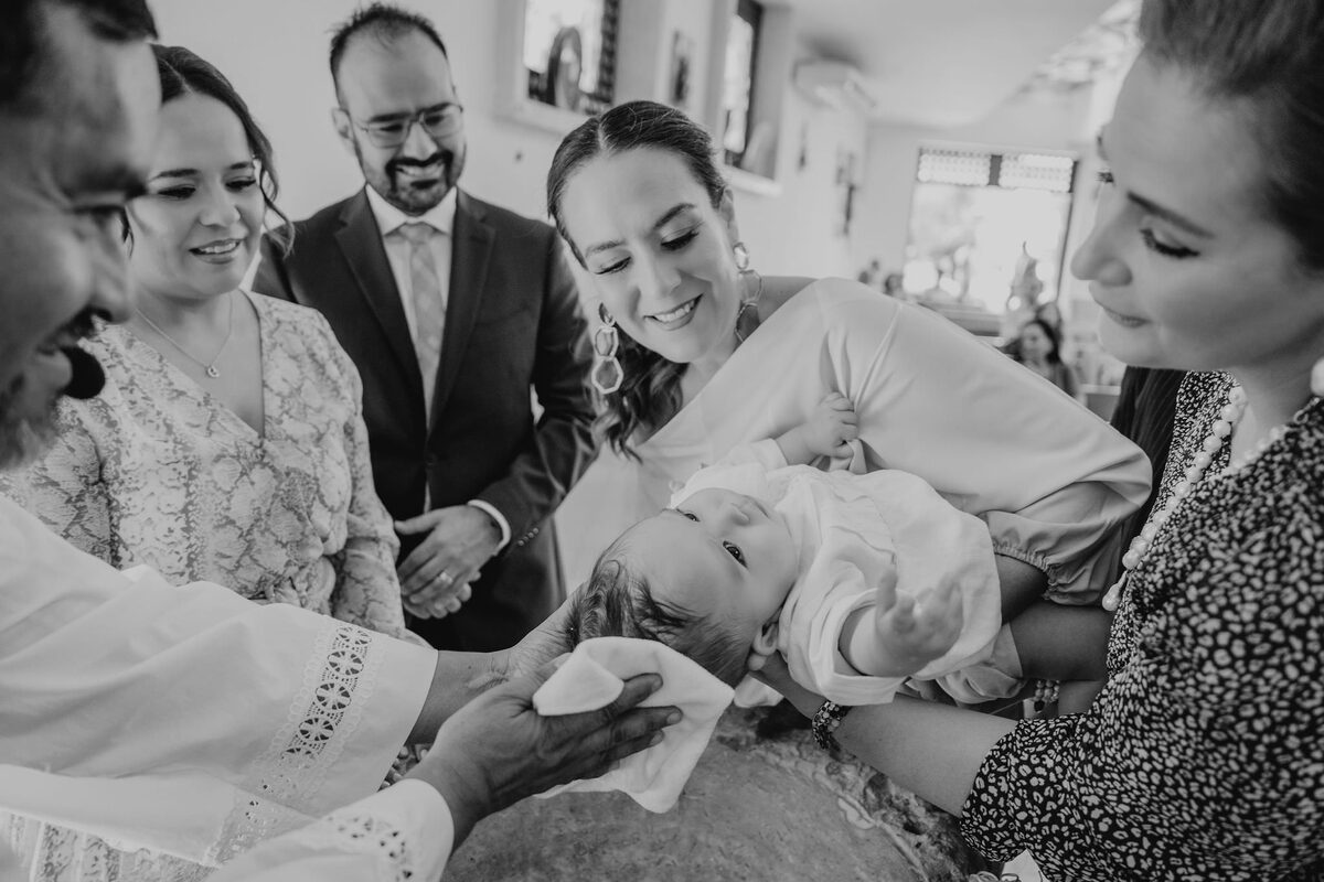 Momento del bautizo, el sacerdote bendice al bebé rodeado de la familia