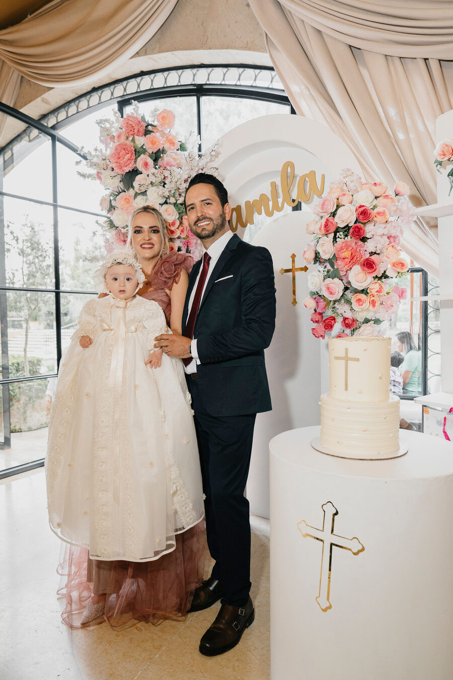 Papás con su bebé junto al pastel de bautizo con cruz