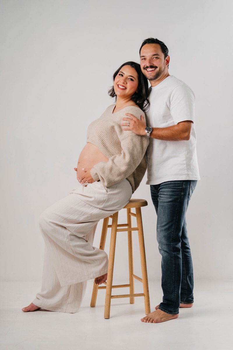Pareja en sesión de embarazo en estudio, mamá en banquito