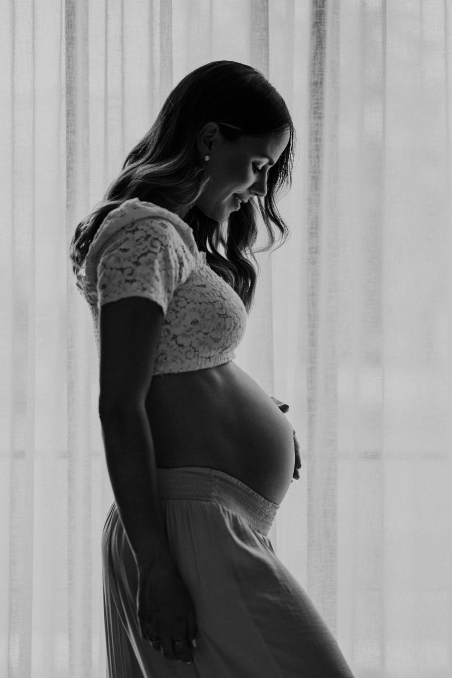 Mamá embarazada de perfil junto a una ventana, fotografía en blanco y negro