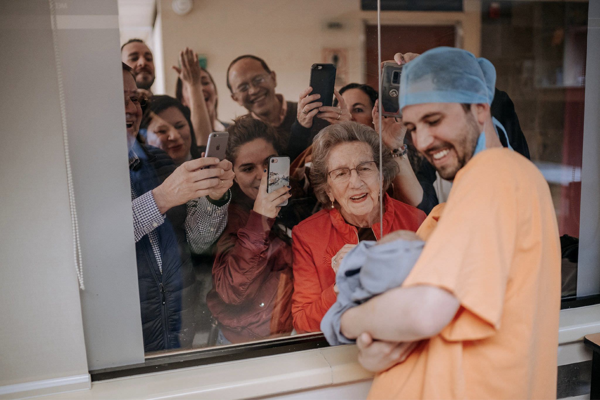 Papá mostrando al bebé recién nacido a través del cristal, familia celebrando afuera